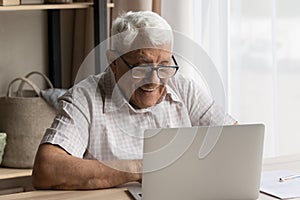 Happy senior older 80s man in glasses using laptop