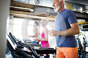 Happy senior people running together on treadmills in gym.