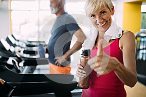 Happy senior people running together on treadmills in gym.