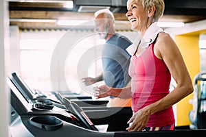 Happy senior people running together on treadmills in gym.