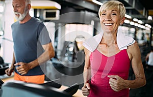 Happy senior people running together on treadmills in gym.