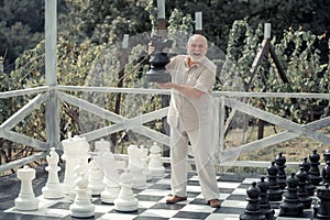 Happy senior playing chess on big chessboard in the park. Retirement. Chess game for old man. Older grandfather, grandpa