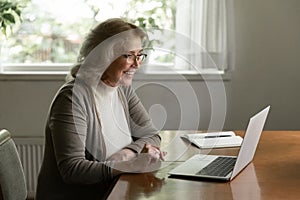 Happy senior retired 60s woman using online app on laptop