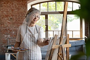Happy senior retired lady drawing in paints on canvas