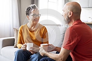 Happy Senior Spouses Chatting And Drinking Coffee Together At Home