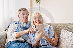 Happy senior spouses surfing internet on cellphone
