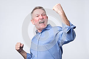 Happy senior strong man, raising clenched fists in hooray gesture, triumphing