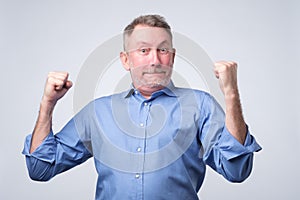 Happy senior strong man, raising clenched fists in hooray gesture, triumphing