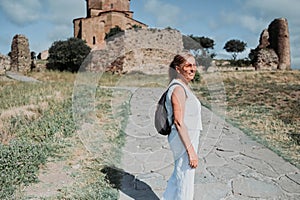 Happy senior traveling mature woman backpacker tourist outdoors in ancient Europe fortress ruins. Retired people summer