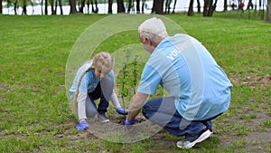 Happy senior volunteer and smiling female kid planting tree together, ecology