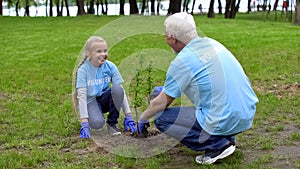 Happy senior volunteer and smiling female kid planting tree together, ecology