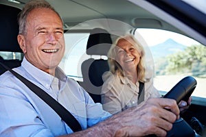 Happy senior white couple driving in their car, smiling to camera, side view, close up