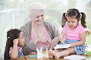 Happy senior woman assisting granddaughters in making handicraft at home