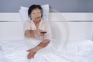 Senior woman in bed with remote control and watching tv