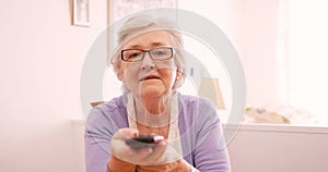 Happy senior woman changing channel with remote control