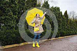 Happy senior woman, cheerful mature, elderly, retired woman with yellow umbrella enjoying life at rainy day in park