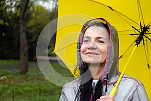 Happy senior woman, cheerful mature, elderly, retired woman with yellow umbrella enjoying life at rainy day in park