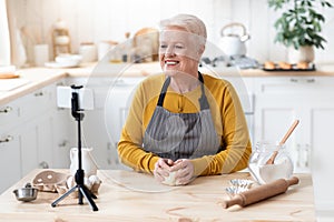 Happy senior woman chef kneading dough and broadcasting