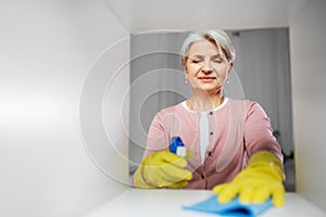 Happy senior woman with cloth dusting rack at home