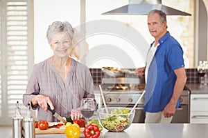 Happy senior woman cutting vegetables with husband in background