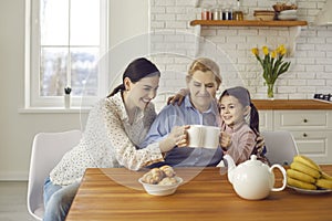 Happy senior woman drinking tea with daughter and granddaughter sitting at home in the kitchen.