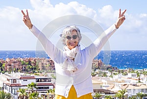 Happy senior woman enjoying sea holiday in winter. Positive, optimistic active retiree smiling with arms up