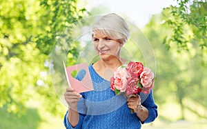 Happy senior woman with flowers and greeting card