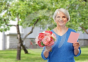 Happy senior woman with flowers and greeting card