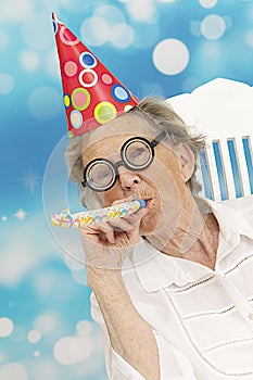 Happy senior woman with funny glasses a party hat and a noise maker