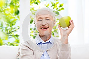 Happy senior woman with green apple at home