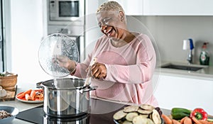 Happy senior woman having fun preparing lunch in modern kitchen - Hispanic Mother cooking for the family