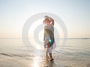 Happy senior woman having fun and splashing water at seashore at sunset