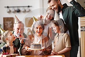 Happy senior woman holding cake with burning candles while celebrating birthday with big lovely family