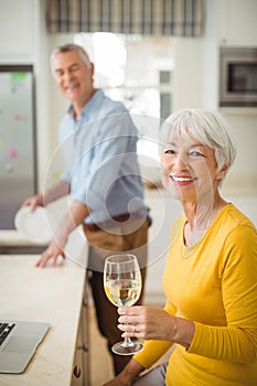 Happy senior woman holding glass of wine in kitchen