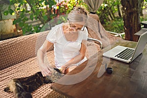 Happy senior woman with home cat use wireless headphones working online with laptop computer outdoor