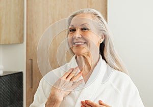 Happy senior woman looking at her reflection in the mirror in morning in the bathroom