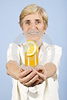 Happy senior woman offer a glass with orange juice