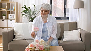 Happy senior woman putting flowers to vase at home