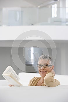 Happy Senior Woman Reading Book On Sofa