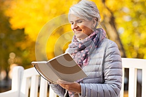 Happy senior woman reading diary at autumn park