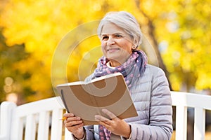 Happy senior woman reading diary at autumn park