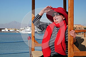 Happy senior woman in red hat and sunglasses waiting your a cruise ship in marina