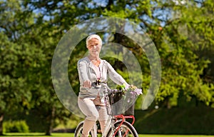 Happy senior woman riding bicycle at summer park