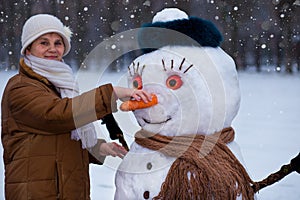 Happy senior woman sculpt and hug a big real snowman in winter