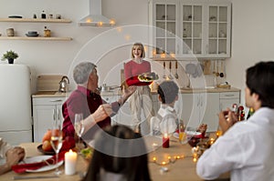 Happy senior woman serving holiday turkey for big extended family, celebrating Thanksgiving or Christmas at home