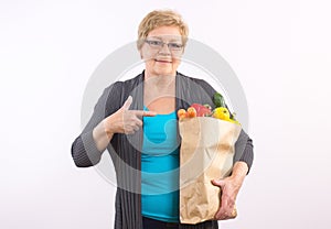 Happy senior woman showing shopping bag with fruits and vegetables, healthy nutrition in old age