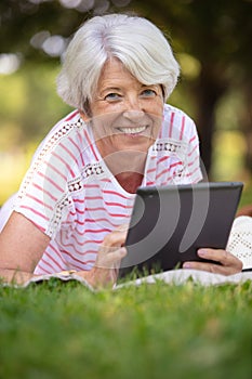 happy senior woman sitting in grass with tablet