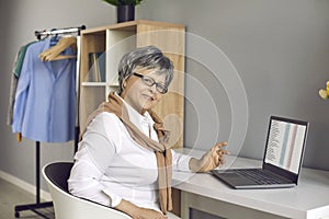 Happy senior woman sitting at her desk at home and working on her laptop computer