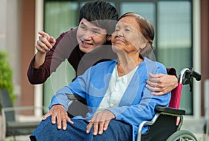 Happy senior woman sitting in wheelchair with young man grandson at outside house