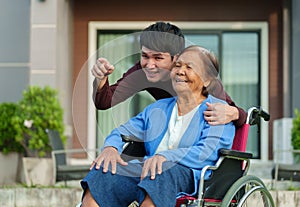 Happy senior woman sitting in wheelchair with young man grandson at outside house